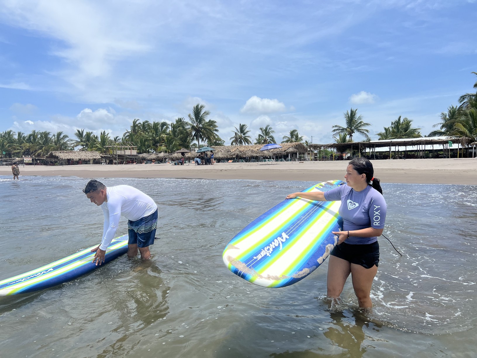 Dos alumnos entrando al agua con sus tablas para practicar lo aprendido